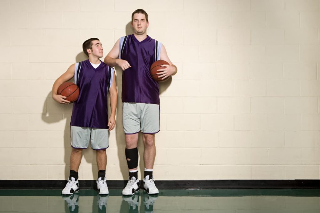 Father standing taller next to his son on the basketball court with son wondering if he can grow taller than his dad