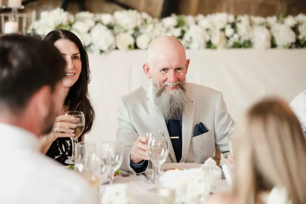 Father, who is best man at a wedding, sitting down at table socialising