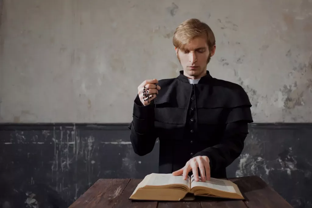 Young preist doing prayers at a wooden table while holding a cross