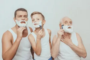 Three generations of men looking in the mirror shaving