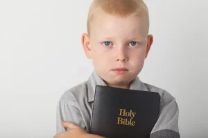 Young child holding a bible in arms being forced to go to church by his parents