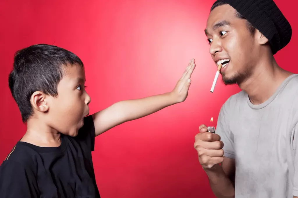 Son asking his dad to stop smoking by putting his hand in front of his father's lighter