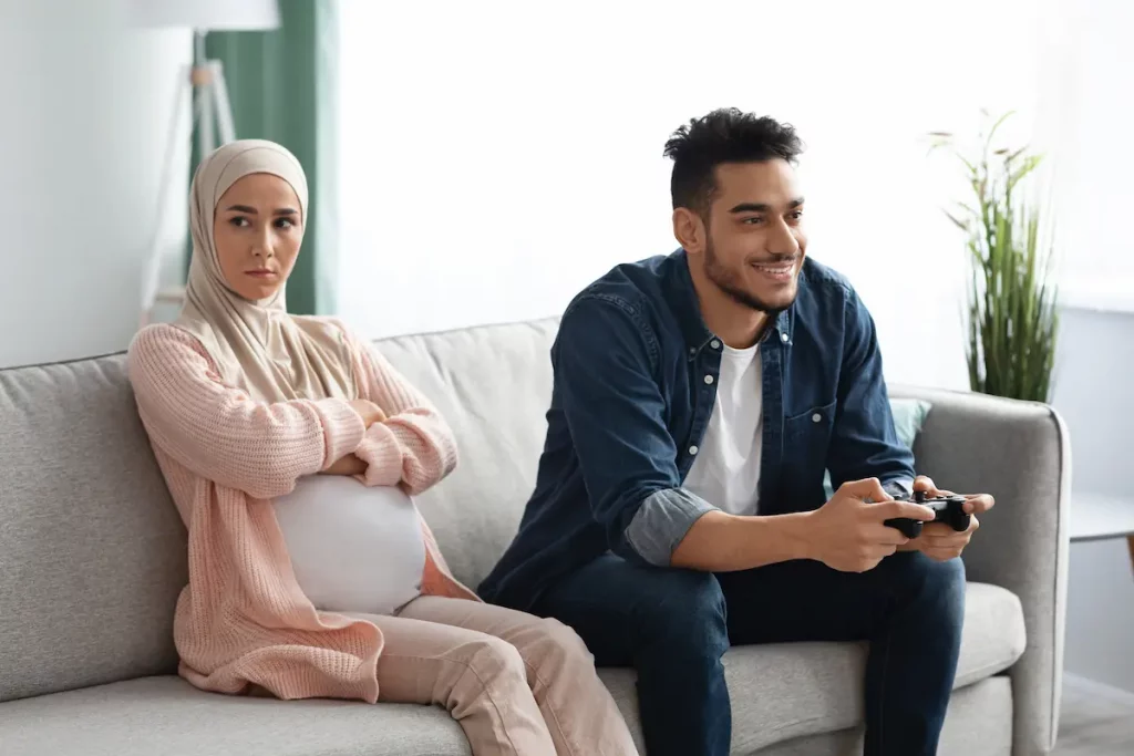 An angry wife sitting next to husband on couch threatening to leave his husband because of video games