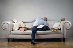 Tired husband sleeps on the couch with open books surrounding him