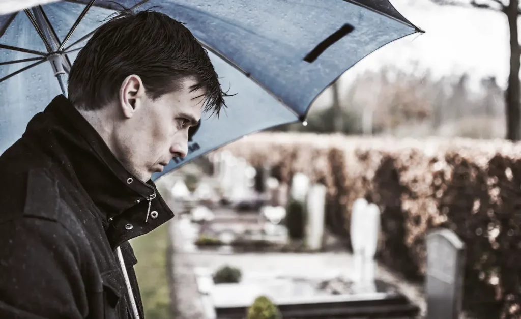 Grieving man standing at grave in the rain since his father died before birth