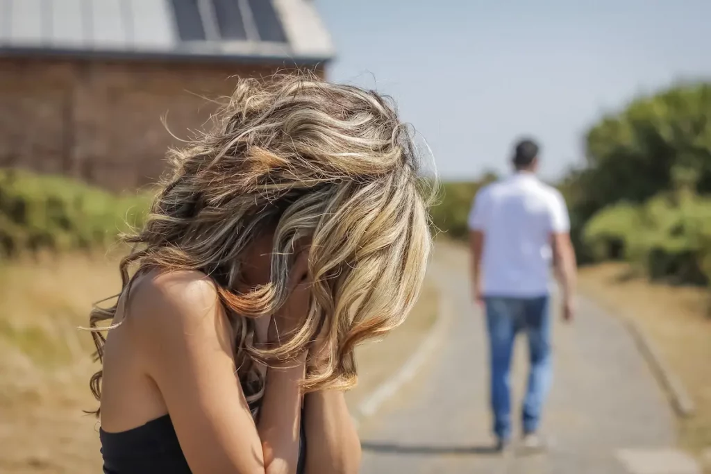 Husband walking away in distance to avoid seeing his wife cry who is standing with hands over face