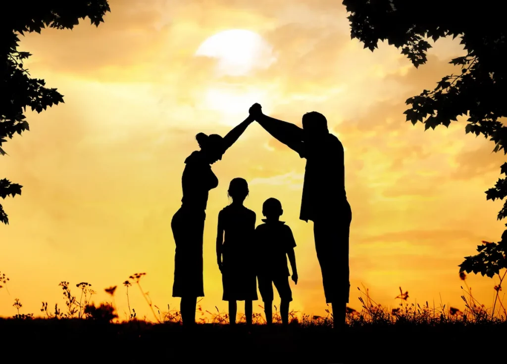 Silhoutte showing co-parenting with parents putting arms together overtop of standing children to show working together and happy family