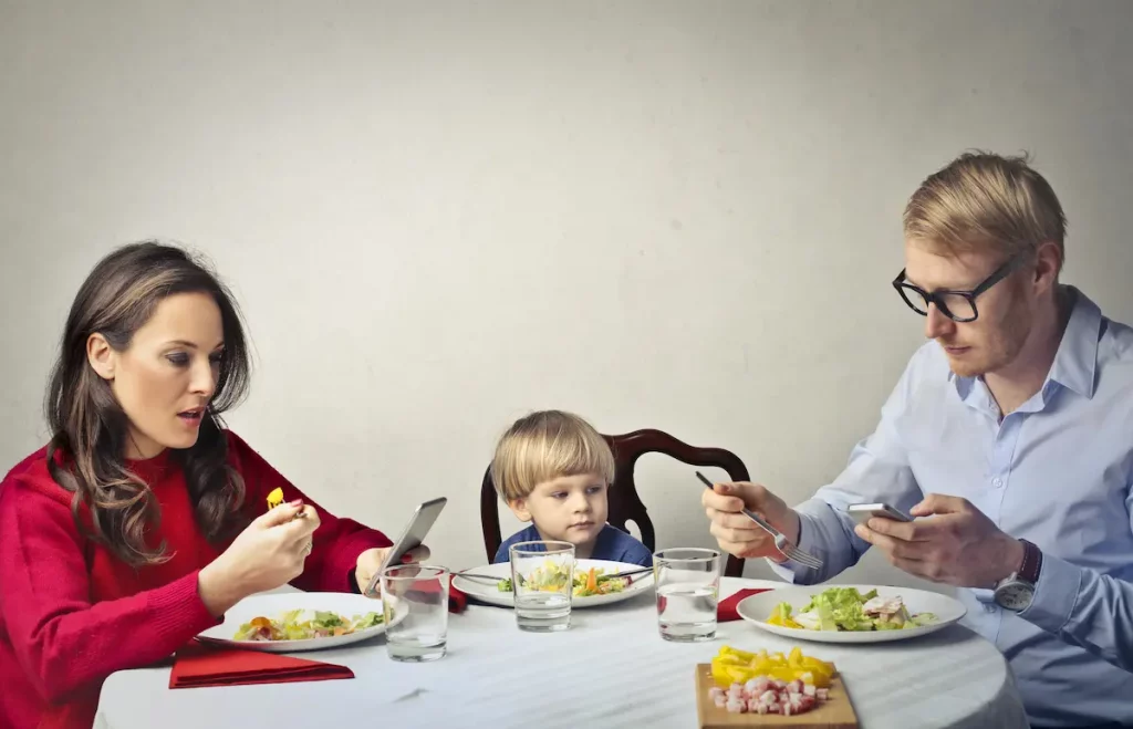 Uninvolved neglectful parents on their phones at dinner table ignoring little boy