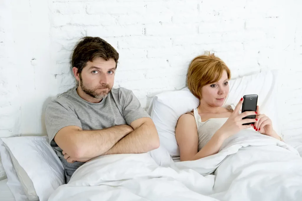 Husband upset with wife in bed because she won't come onto him and instead plays on phone