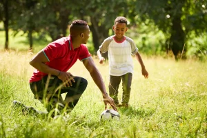 soccer dad holding ball for son to kick on grass