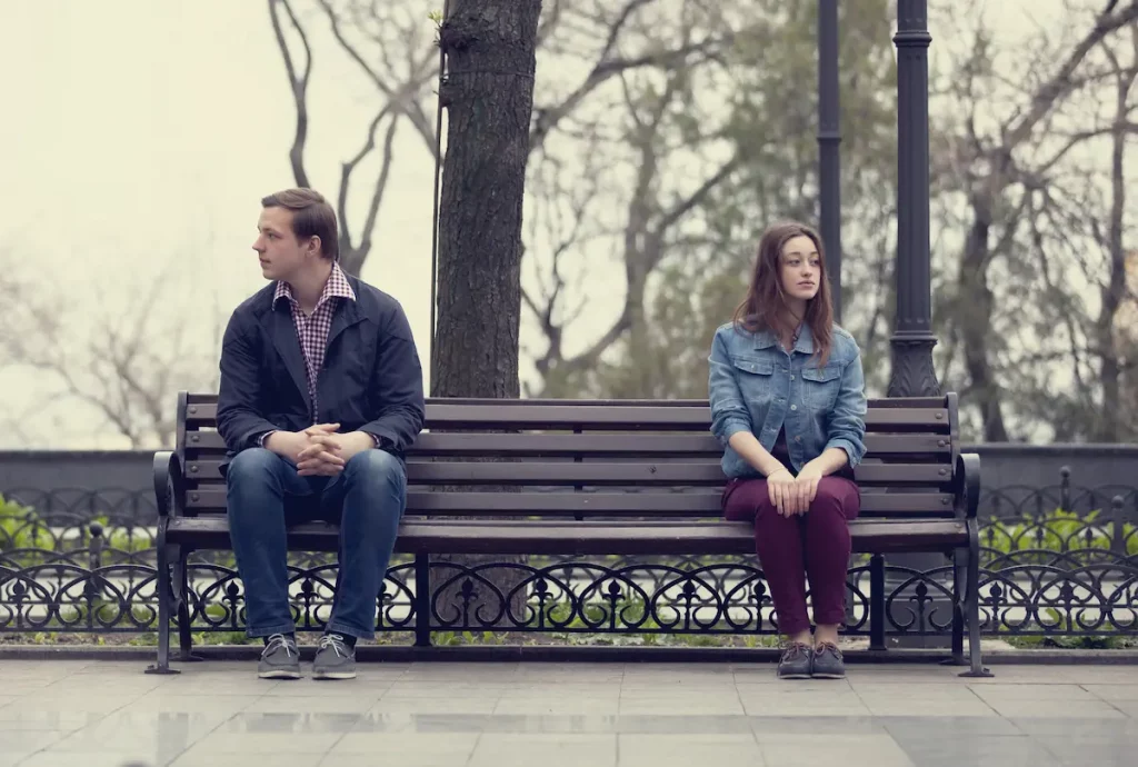 young man and woman sitting on same bench with distance between