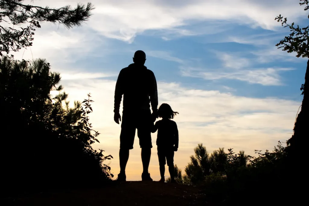 Picture of father and daughter holding hands in shadows with sunset background
