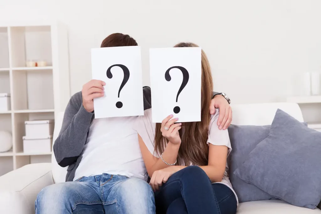 couple on couch holding question marks over face wondering if marriage is really worth it