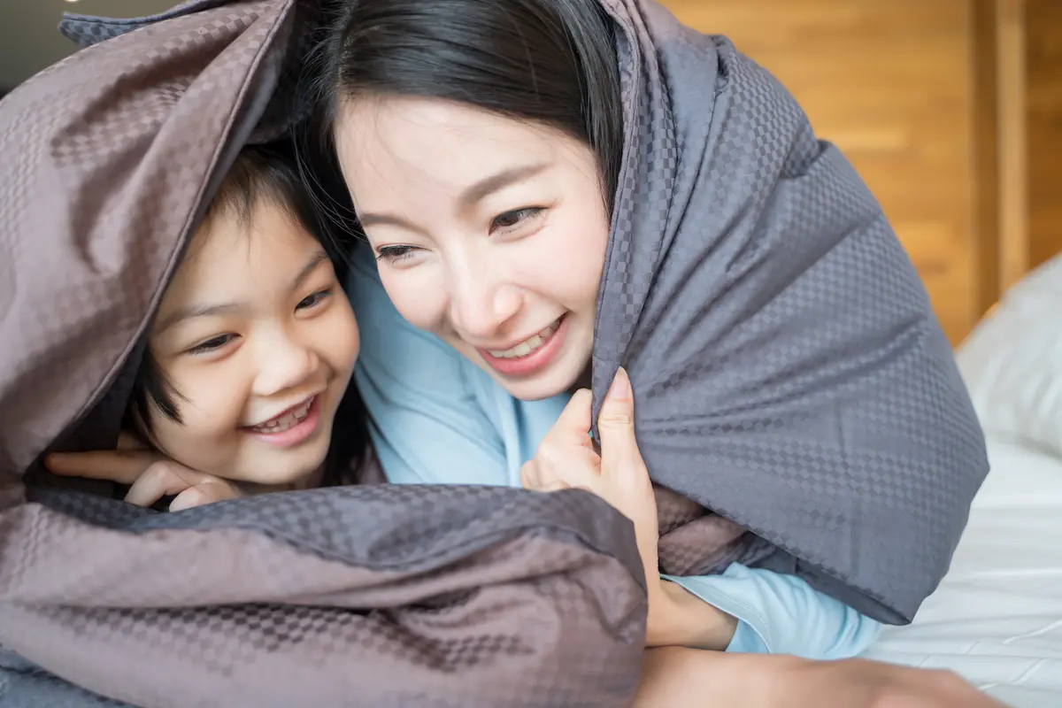 Mother and daughter under covers laughing