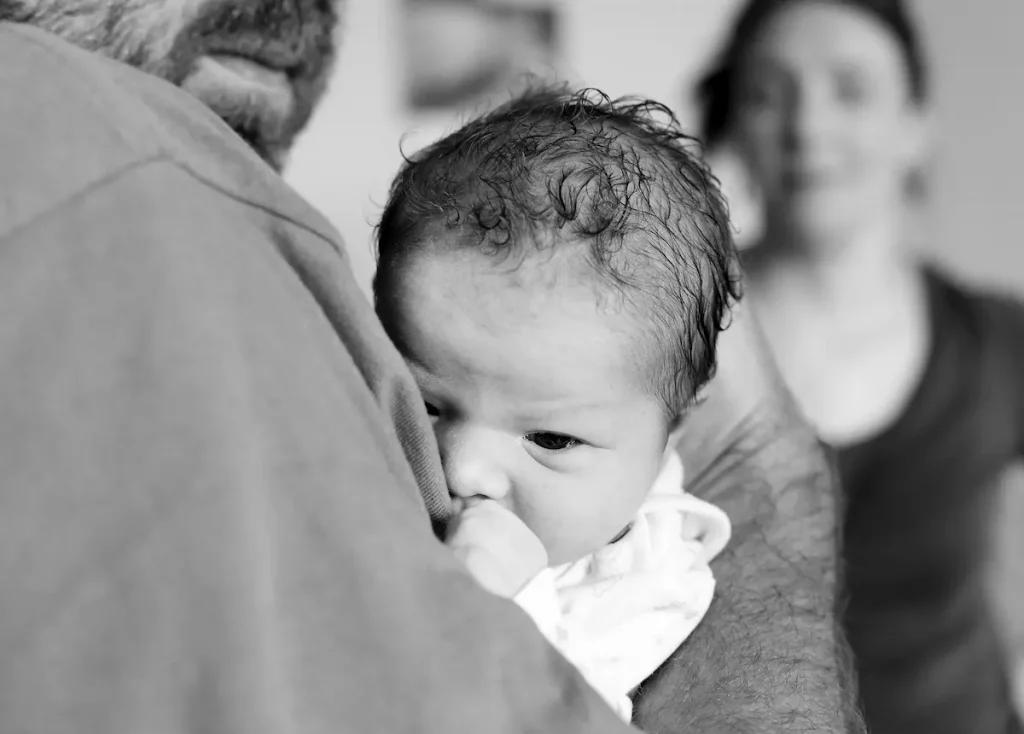 Upclose of newborn being held by father and mother in background