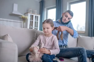 A father doing his daughter's hair on couch while talking on phone