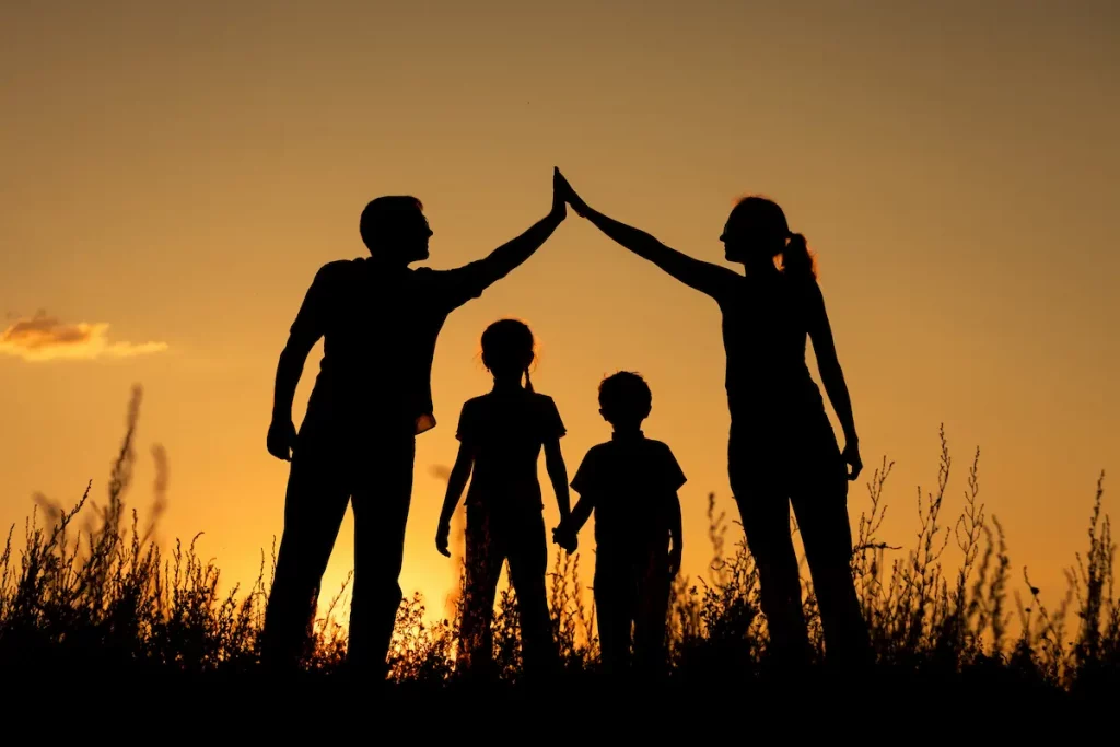 Silhoutte showing co-parenting with parents putting arms together overtop of standing children to show working together and happy family