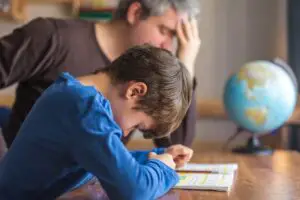 Son holding head down looking sad while frustrated father looks away during homework
