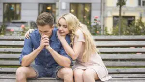 Girlfriend encouraging upset boyfriend on bench in park
